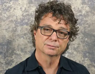 A man with curly hair and glasses is posing for the camera.