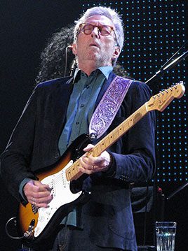 A man in black jacket playing guitar on stage.